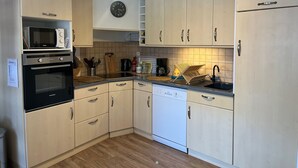 A kitchen with light wood cabinets, a microwave, oven, dishwasher, and a clock on the wall.