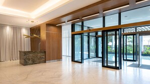 Un vestíbulo amplio con un mostrador de recepción de mármol, paneles de madera y puertas de cristal que dan al exterior.
