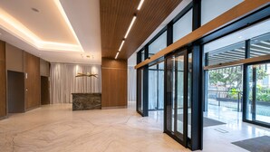 Un vestíbulo amplio con suelo de mármol, paneles de madera, un mostrador de recepción y grandes puertas de cristal que dan a un espacio exterior.