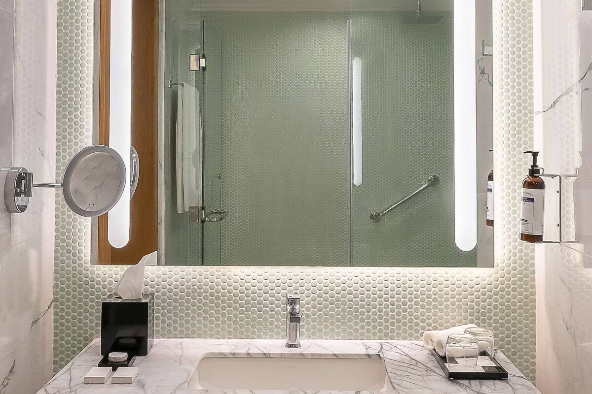 A modern bathroom with a marble sink, a large mirror, and a glass shower enclosure.