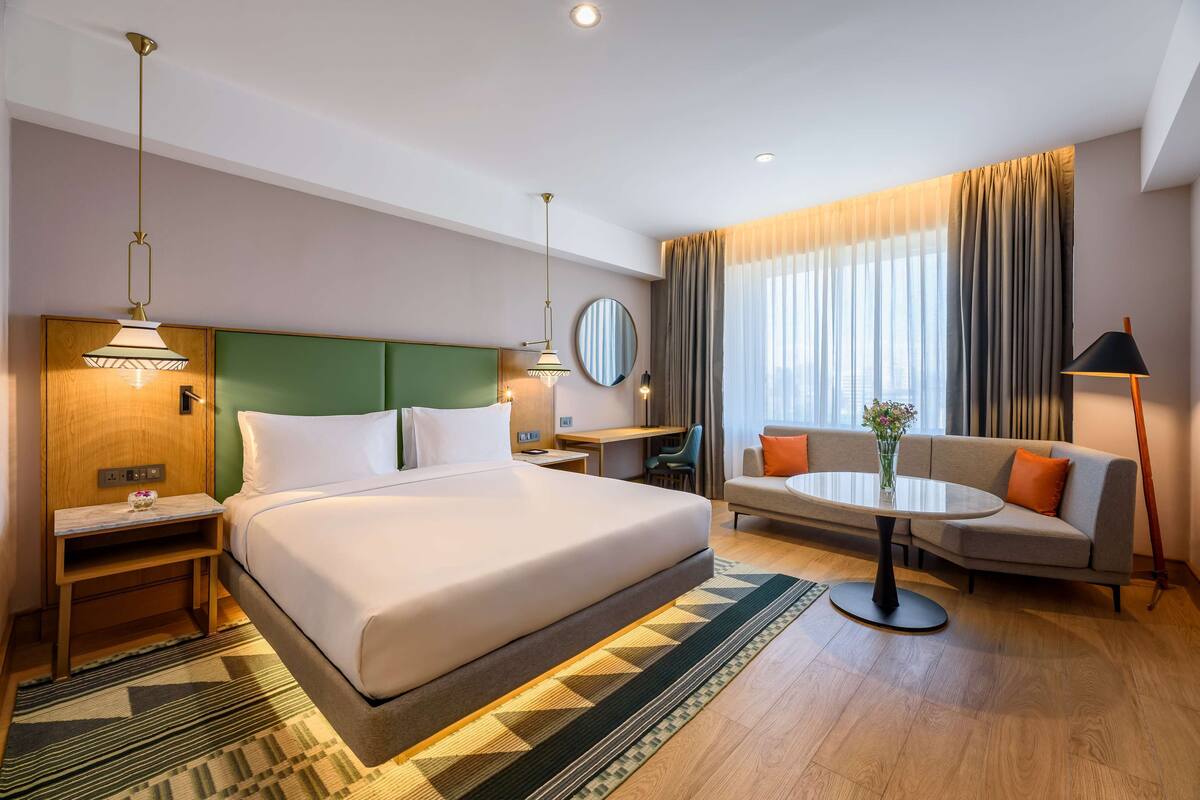 A hotel room with a large bed, a sofa, a small table, a desk, and a mirror.