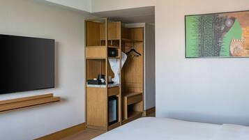 A hotel room with a bed, a TV mounted on the wall, a wooden wardrobe, and a painting on the wall.