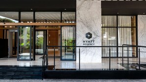 Entrada moderna de un hotel Hyatt Regency con puertas de vidrio, una columna de mármol y una escalera.