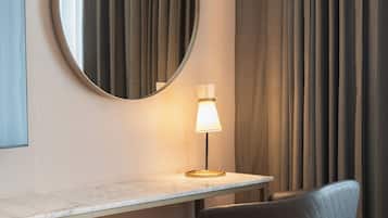Una habitación de hotel con un espejo redondo, un escritorio con lámpara, una silla y una cama.