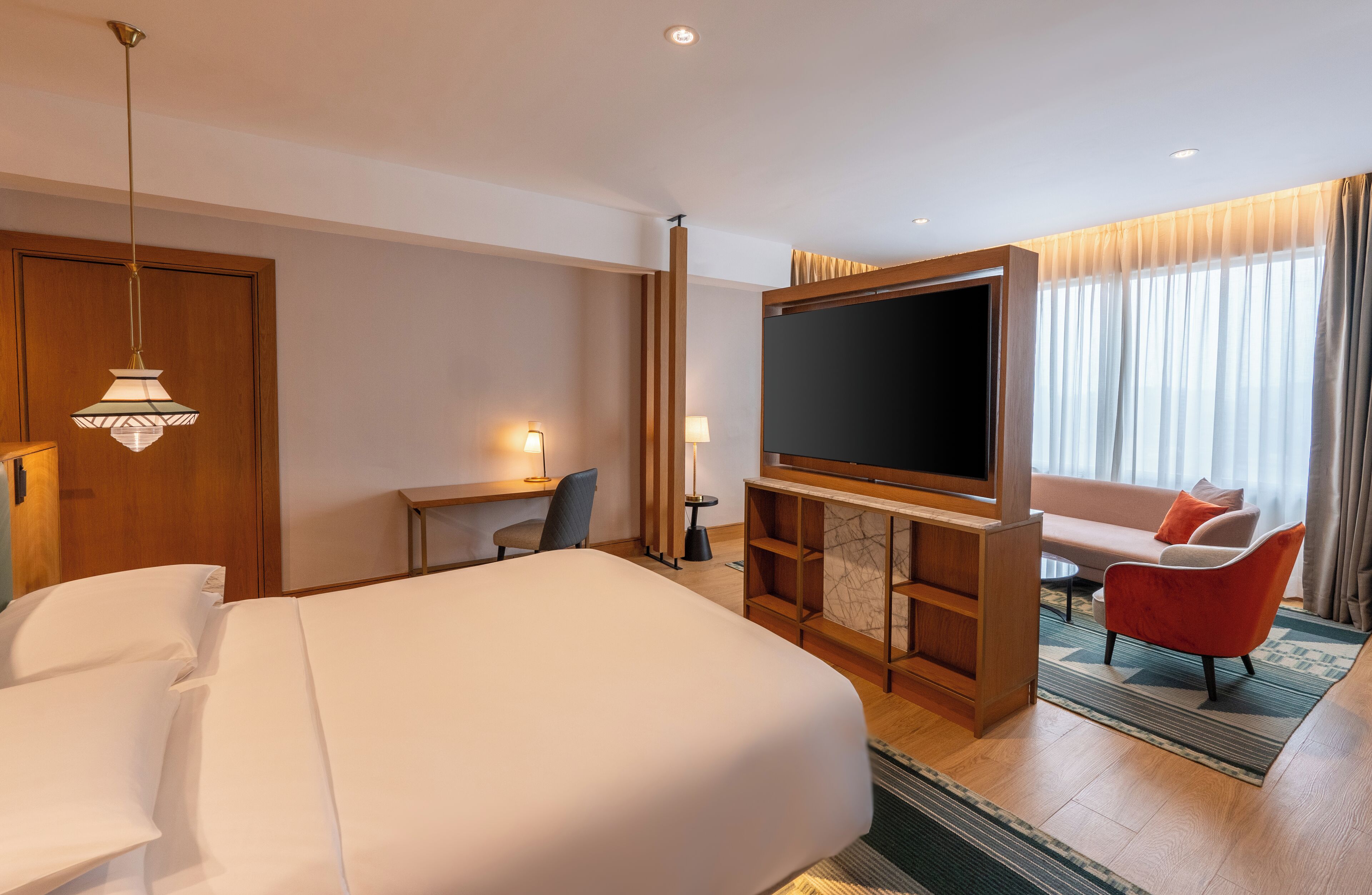 A hotel room with a large bed, a desk with a chair, a television, and a sofa.