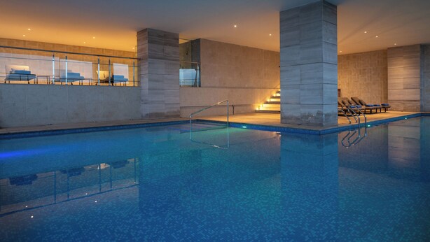 Una piscina interior moderna con agua cristalina, sillas de descanso y barandilla de vidrio.