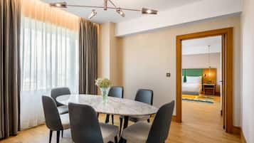 A hotel room with a dining area featuring a marble table, grey upholstered chairs, and a modern chandelier.