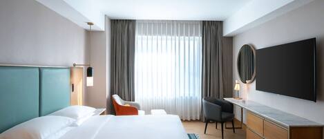 Een hotelkamer met een groot bed, een bureau, een stoel, een televisie en een raam met gordijnen.