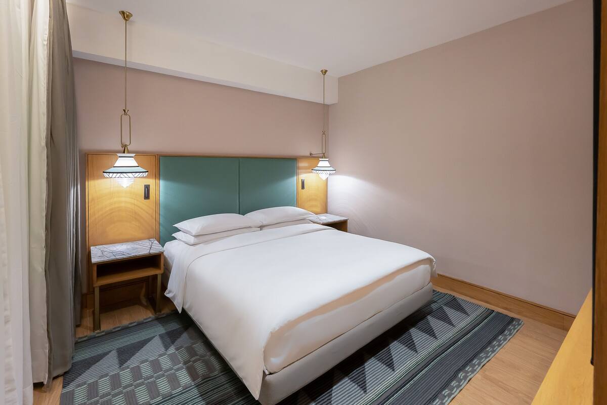 A hotel room with a bed, wooden headboard, bedside tables, and two pendant lights.