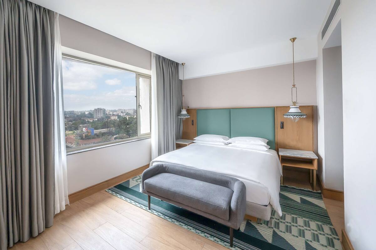 A hotel room with a large bed, a view of the city, and a window with curtains.