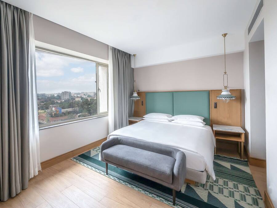 A hotel room with a large bed, a view of the city, and a window with curtains.