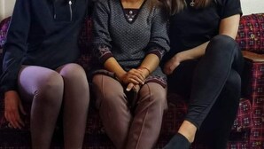 Tres personas sentadas en un sofá estampado en una habitación con dos cuadros colgados en la pared.