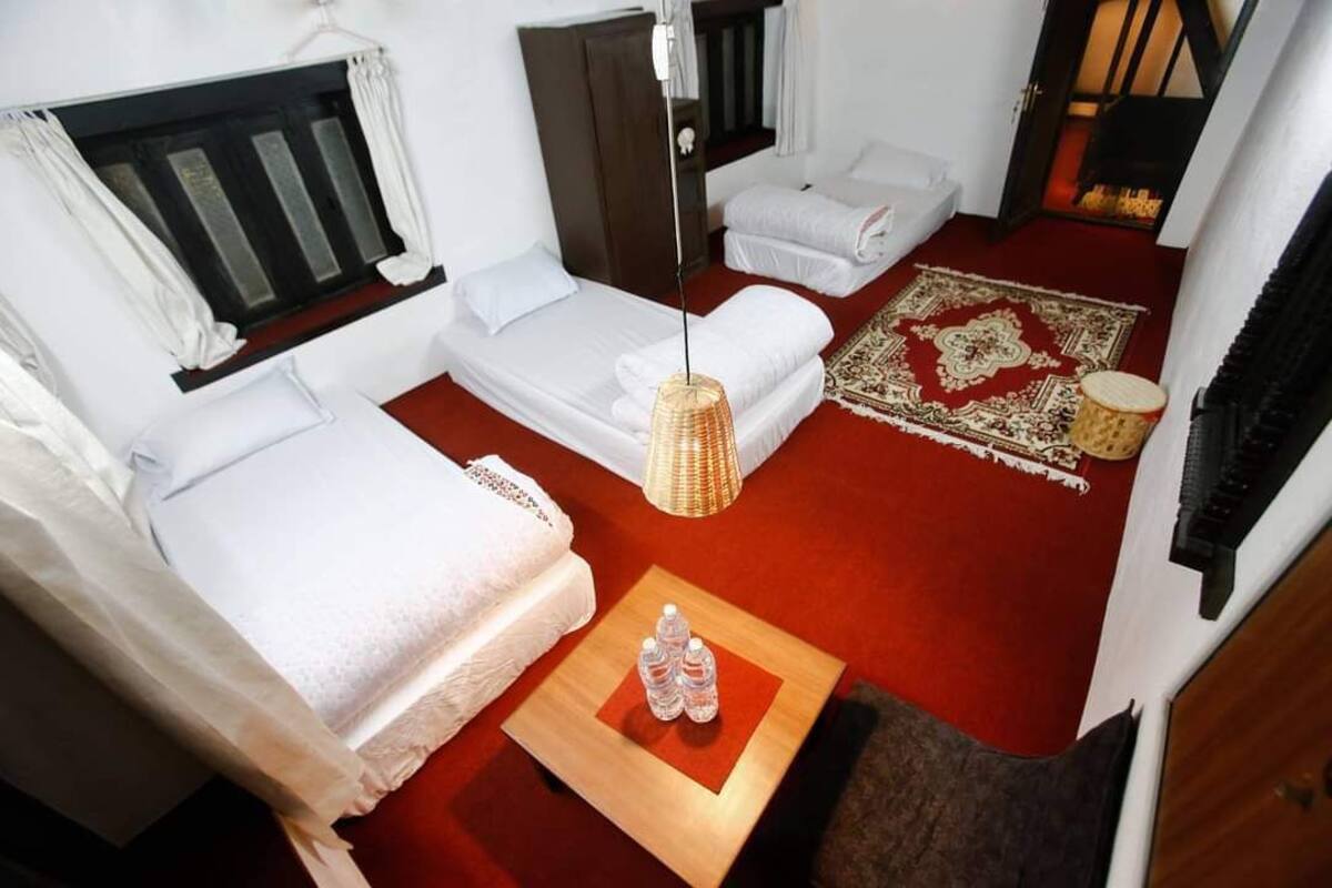 A compact room with two beds, a small table with water bottles, a red carpet, and a decorative rug.