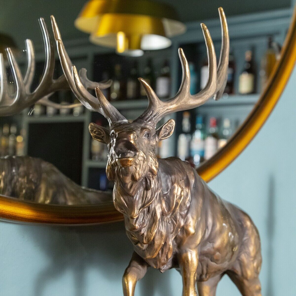 A bronze deer sculpture with antlers, positioned in front of a bar area with shelves of bottles.