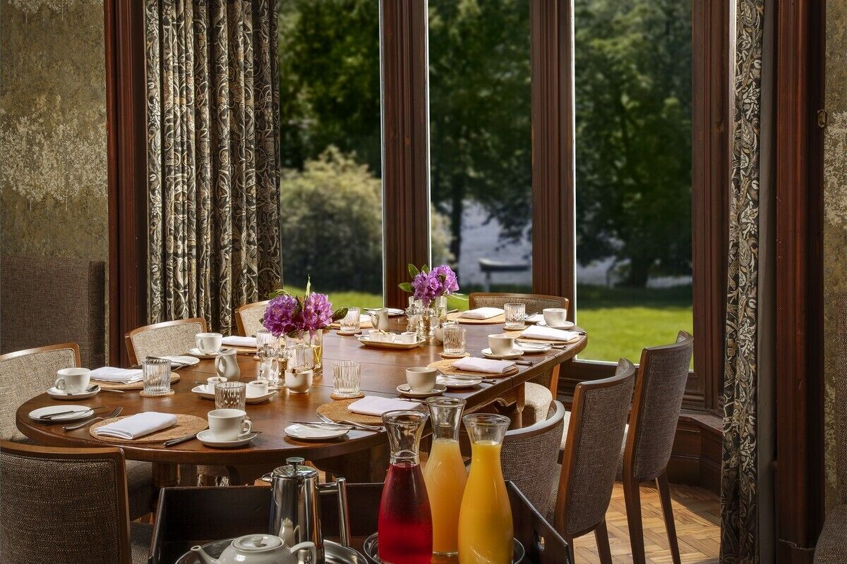 A dining table set for a meal with chairs, a vase with purple flowers, and two bottles of orange juice.