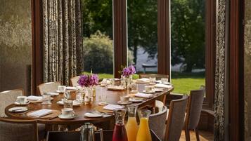 A dining table set for a meal with chairs, a vase with purple flowers, and two bottles of orange juice.