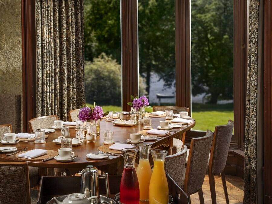 A dining table set for a meal with chairs, a vase with purple flowers, and two bottles of orange juice.