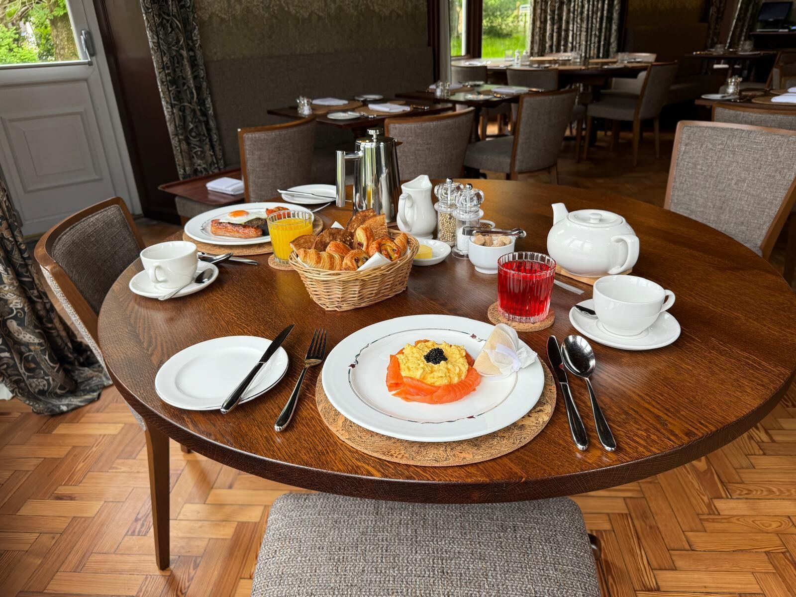 A dining area with a round table set for breakfast, including plates, cutlery, and a basket of bread.