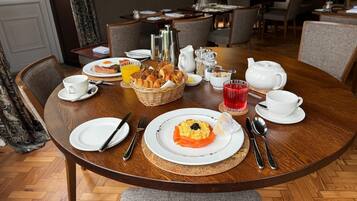 A dining area with a round table set for breakfast, including plates, cutlery, and a basket of bread.