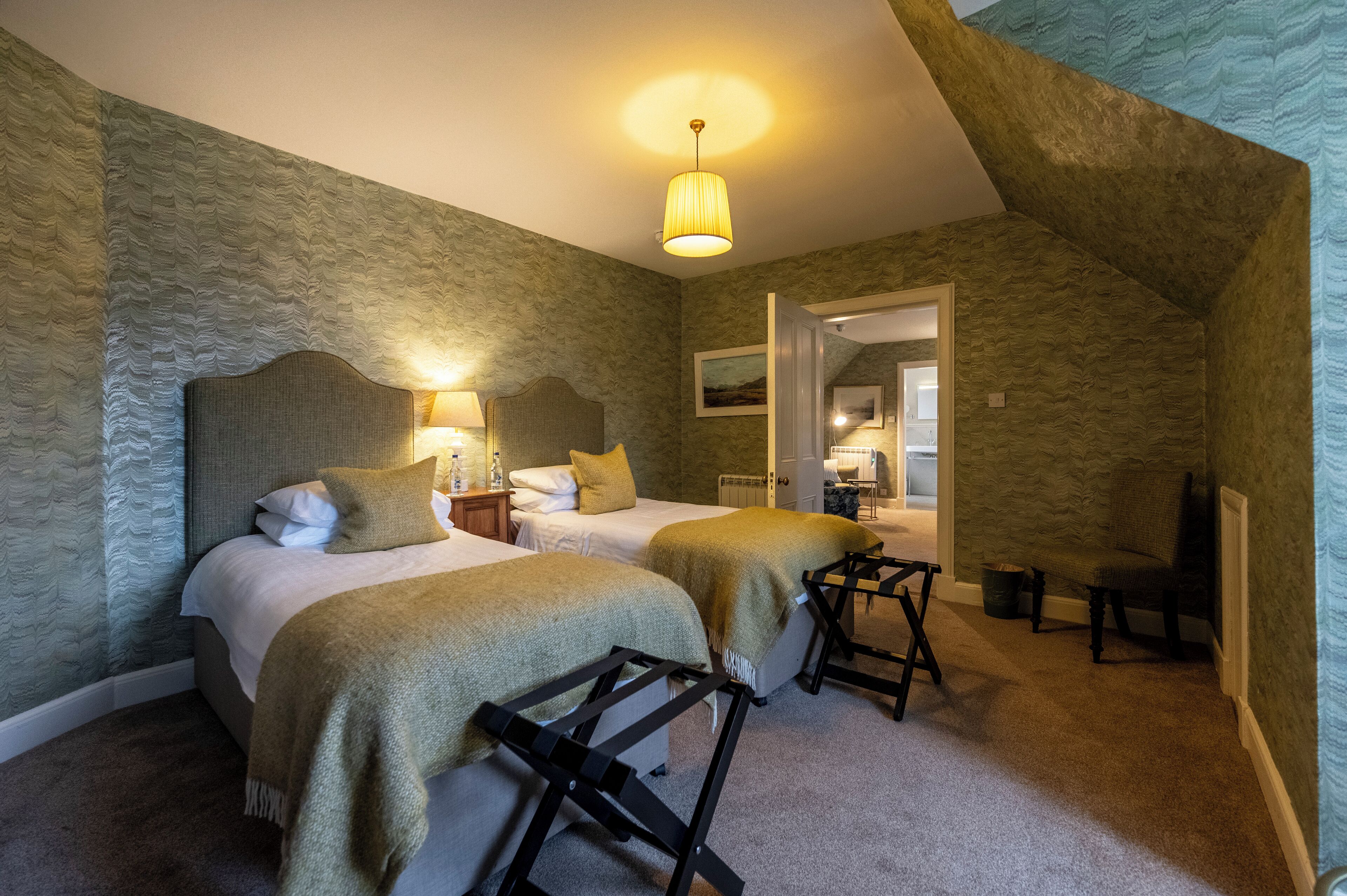 A bedroom with two beds, a nightstand, a chair, and a lamp.