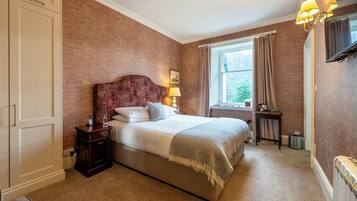 A bedroom with a large bed, a nightstand, a window with curtains, and a radiator.