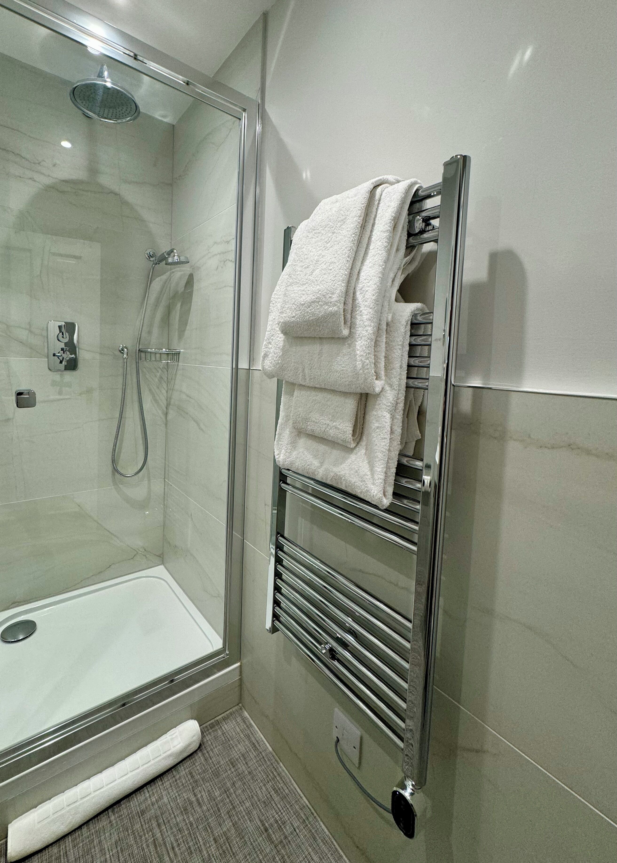 A glass-enclosed shower with a handheld showerhead, a towel rack with folded towels, and a towel bar.