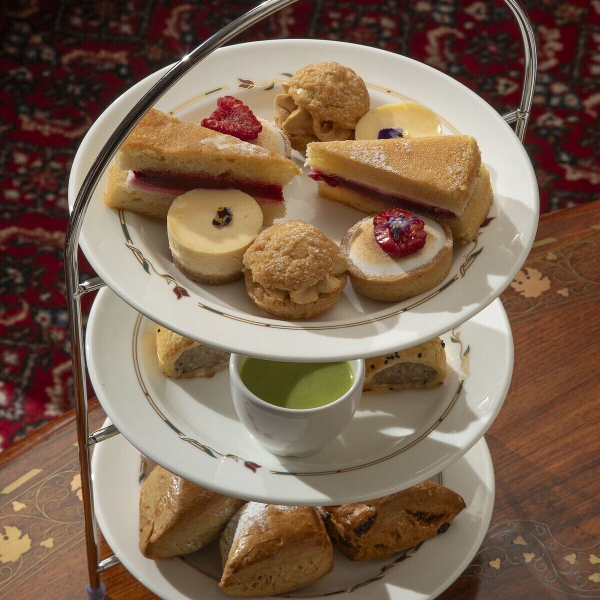 A three-tiered dessert tray with various pastries and a small cup of green tea.