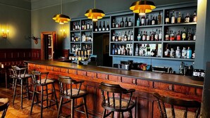 Eine Bar mit Holzbarhocker, einer Theke mit Zapfhahn und Regalen voller Flaschen.