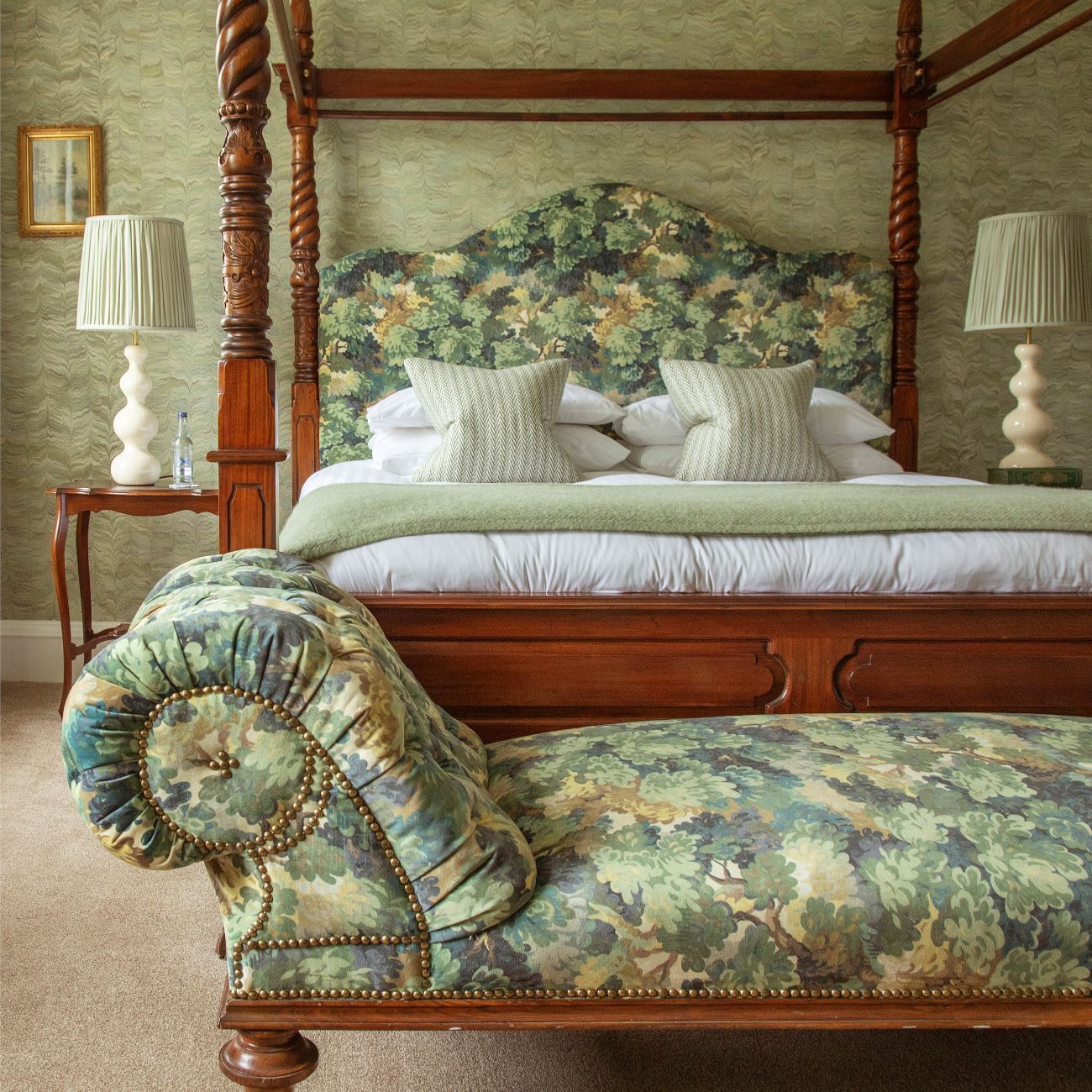 A four-poster bed with a floral headboard, a matching upholstered bench, and two bedside tables with lamps.