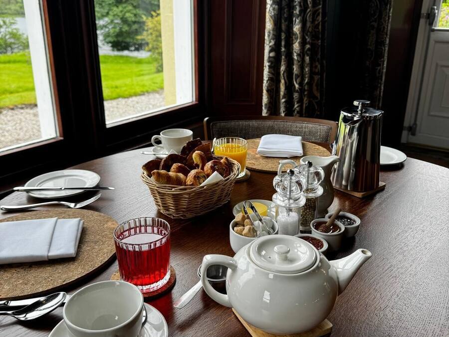 Una mesa de desayuno dispuesta con té, café, croissants y una cesta de pasteles.