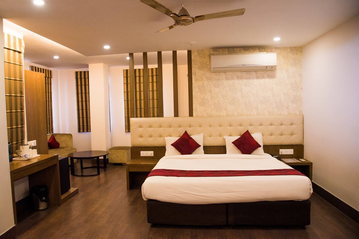 A hotel room with a large bed, a desk, a chair, a small table, and a ceiling fan.