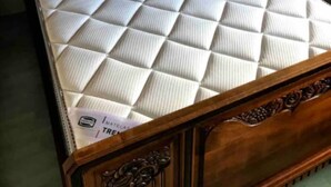 Un lit en bois avec un matelas matelassé et une table de chevet surmontée d’une lampe rouge.