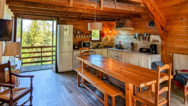 Une cabane en bois rustique comprenant un coin repas, une cuisine et une chambre à l’étage avec une lucarne.