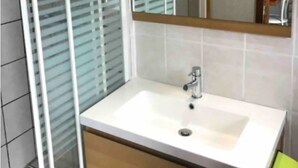Une salle de bain avec un lavabo blanc, un miroir au-dessus et une fenêtre avec des stores.