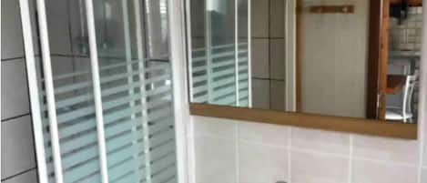 Un baño con lavamanos blanco, un espejo encima y una ventana con persianas.
