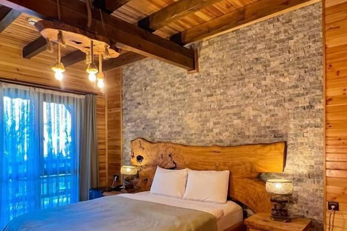 A cozy wooden room with a large bed, stone wall, and a rustic ceiling.