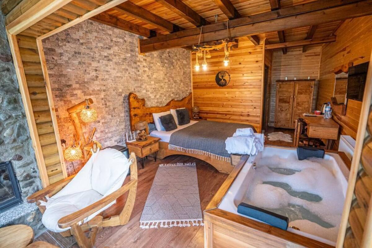 A cozy wooden cabin room with a bed, a chair, a small table, and a bathtub.