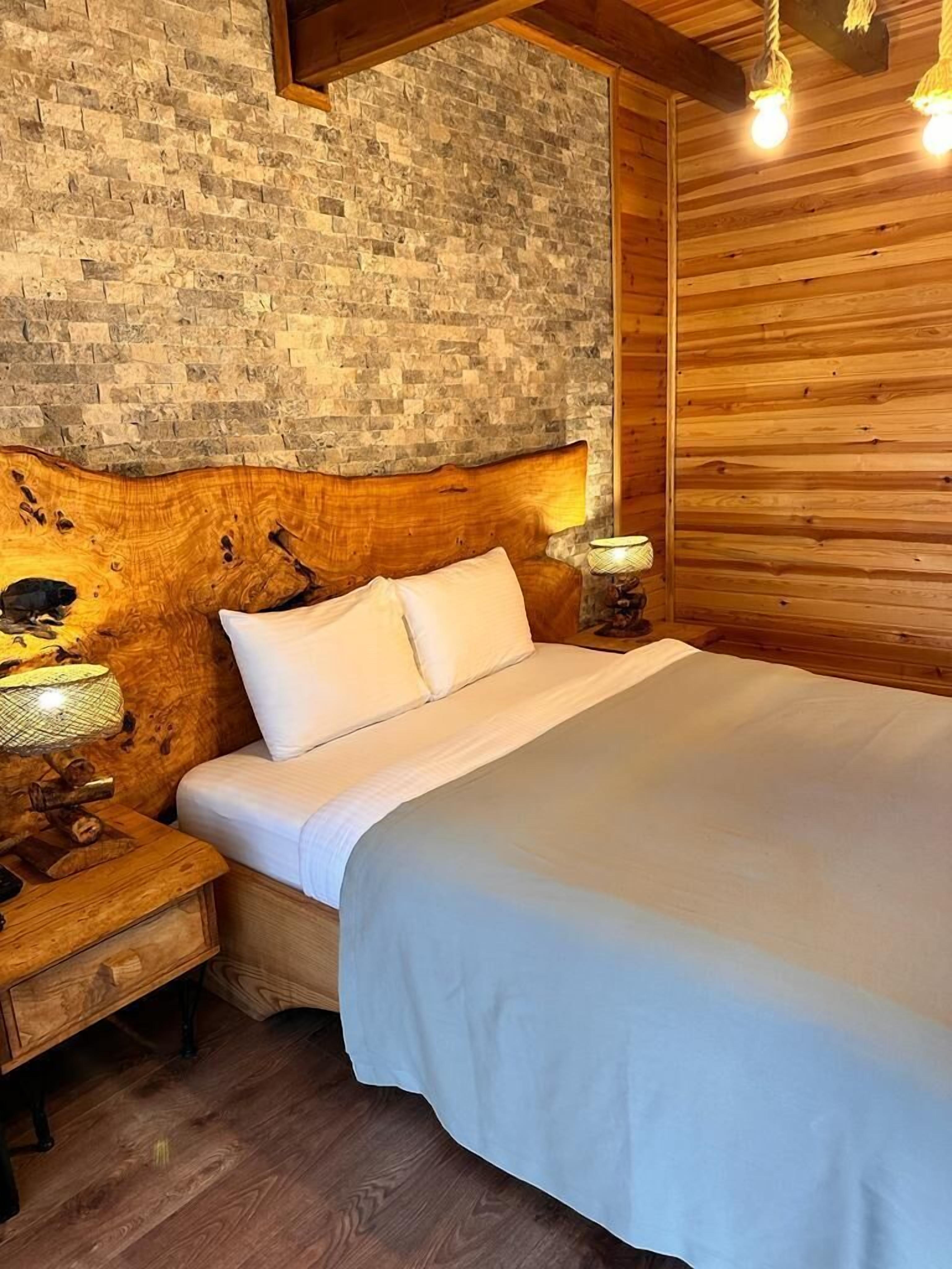 Un dormitorio con pared de piedra, cabecera de madera y cama con ropa de cama blanca.