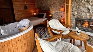 A cozy cabin interior with a stone wall, a wooden ceiling, a stone fireplace, a wooden bathtub, and two wooden chairs with cushions. - Abant Pelit  (Bolu)