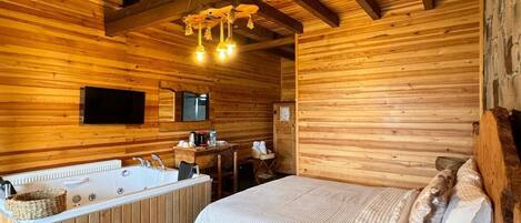Interior de una cabaña de madera con una cama grande, una mesa de madera, un lavabo y una silla de madera.