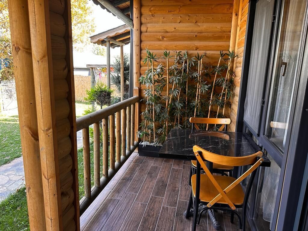 Varanda de madeira com mesa e cadeiras, cercada por plantas de bambu.