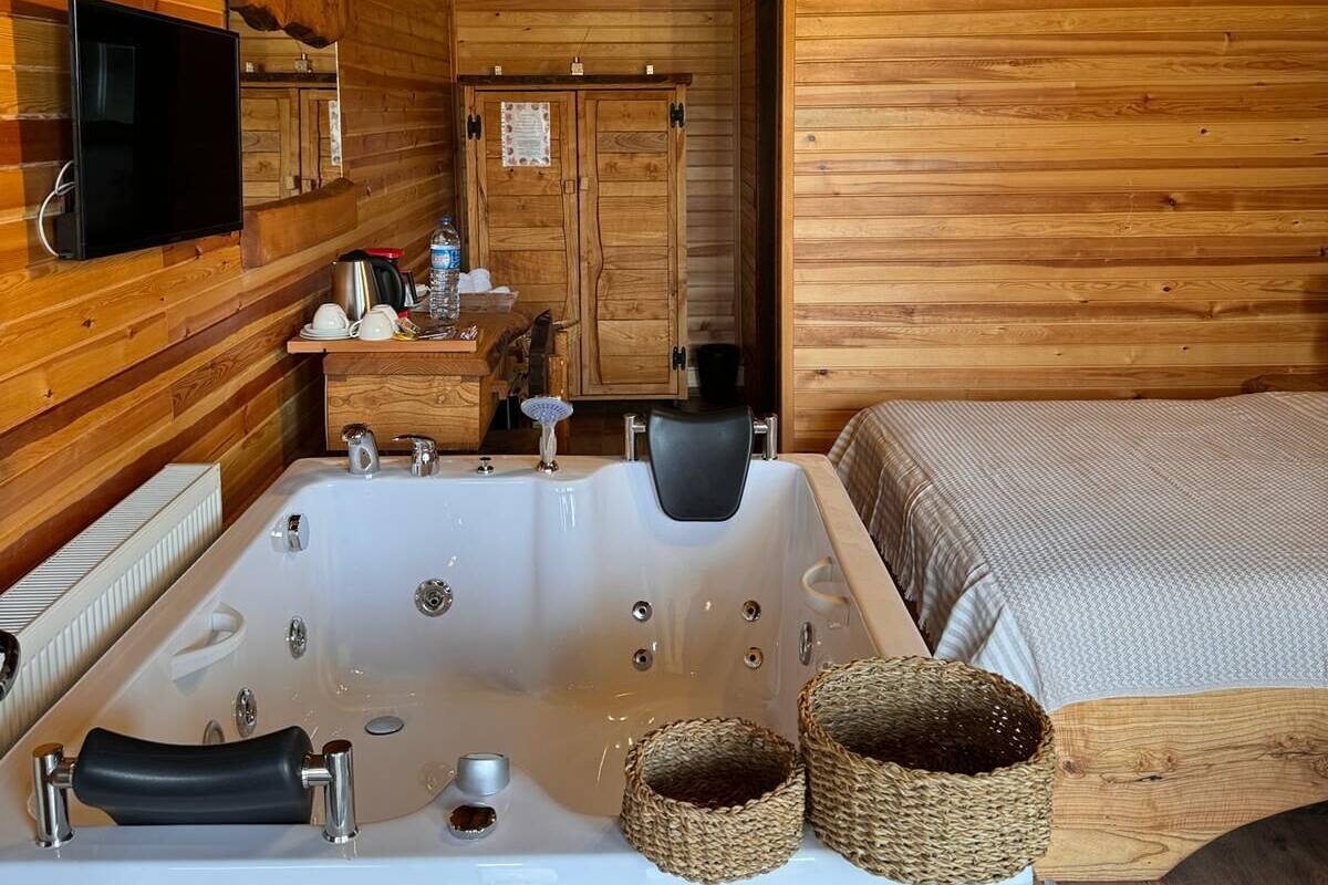 A wooden cabin interior with a large bathtub, a bed, a television, and a wooden wardrobe.