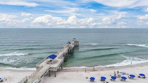 A pier extending into the ocean with beach chairs and umbrellas on the sand. - Four Seasons 804E | Gulf Views + Resort Pools (Orange Beach)