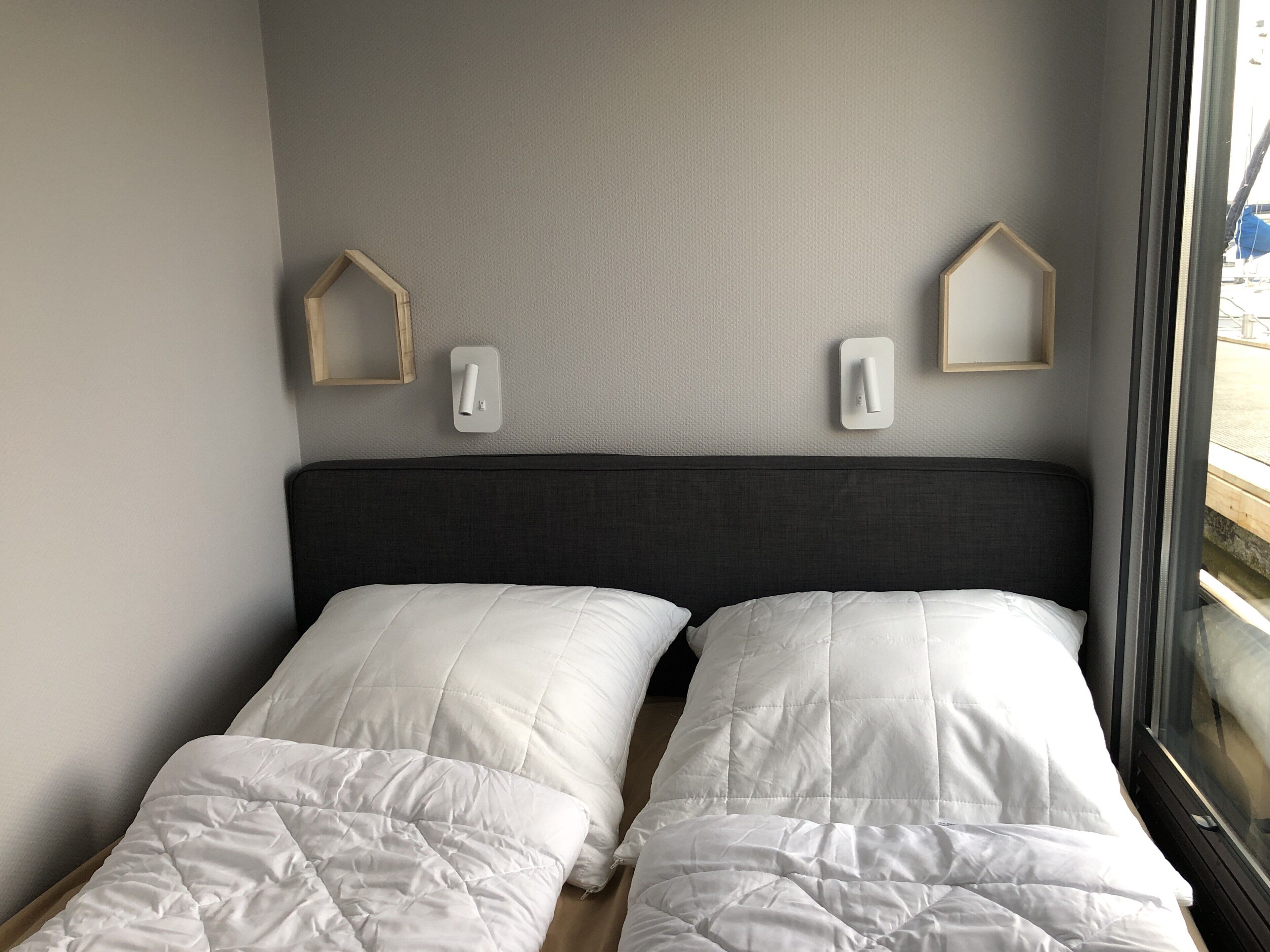 A room with two beds, a dark headboard, and two wall-mounted light switches.