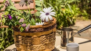En kurvefletkurv med blomster og en metalkop på et bord udendørs.