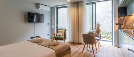 A modern hotel room with a large bed, a desk with a chair, a TV, and a balcony with a view.