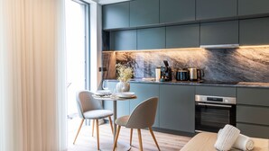Een moderne keuken met donkere kastjes, een marmeren spatwand, en een eethoek met twee stoelen en een tafel.