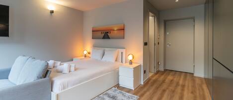 A modern bedroom with a large bed, bedside tables, a painting, and a wooden floor.