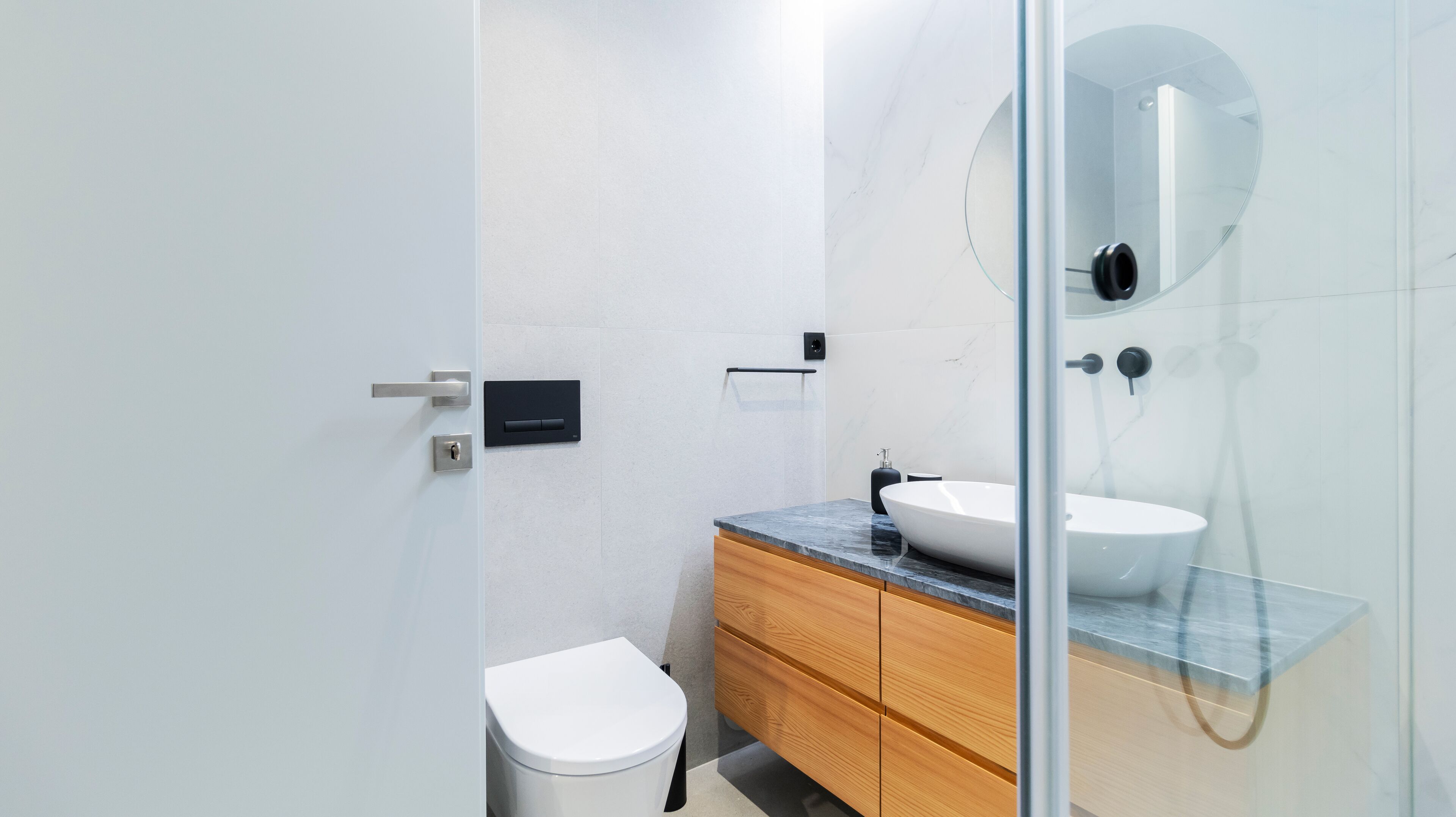 A modern bathroom with a white toilet, wooden vanity, and a glass shower enclosure.