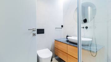 A modern bathroom with a white toilet, wooden vanity, and a glass shower enclosure.